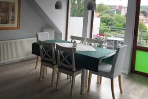 Un coin repas avec une table dressée pour quatre personnes, des chaises blanches, un radiateur et une vue sur la verdure à l’extérieur.