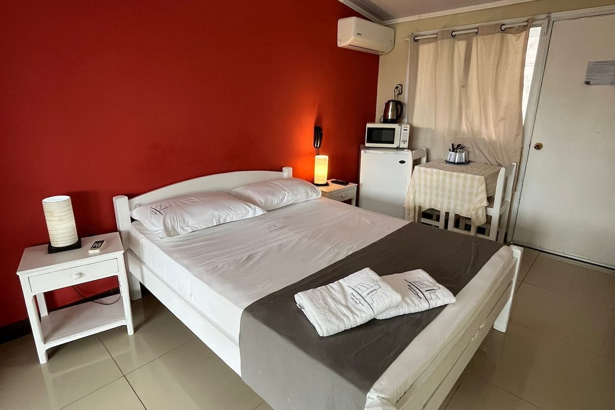 A neatly arranged bedroom with a bed, bedside table, lamp, and a small table with a kettle.