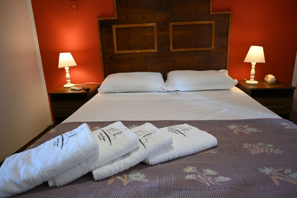 A hotel room with a neatly made bed, two bedside lamps, and a floral-patterned bedspread.
