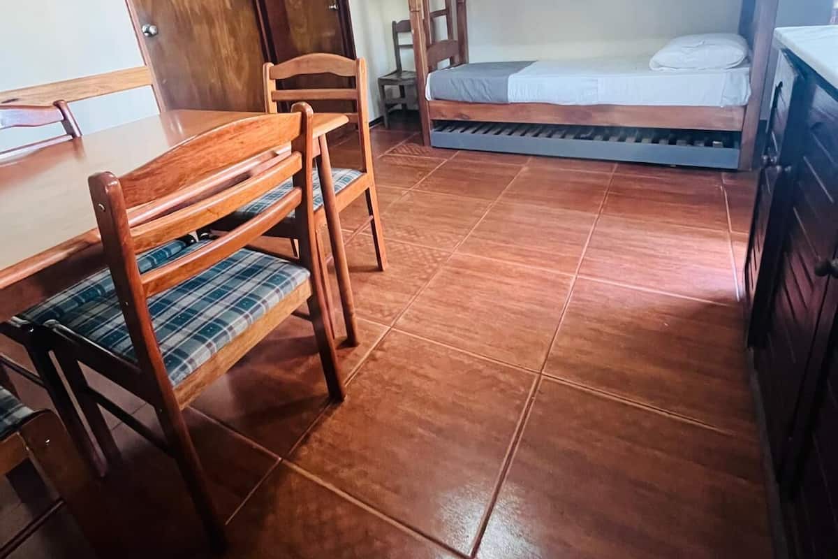 A room with a wooden bunk bed, a wooden desk with a chair, and a tiled floor.