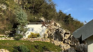 A patio with a wooden table and chairs, surrounded by stone walls and greenery. - Waterfront house Les Roches  (Rochefort-sur-Nenon)