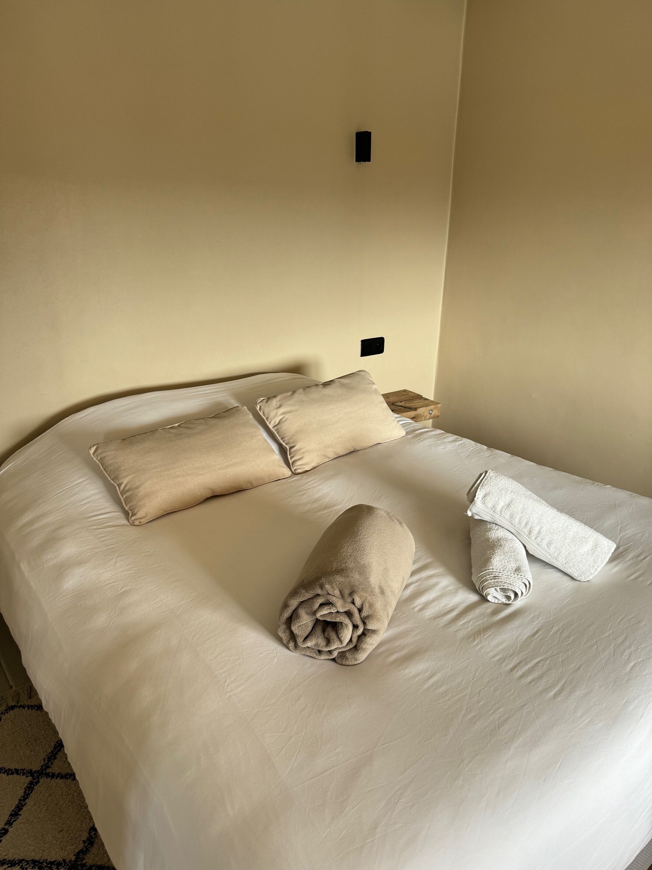 A neatly made bed with beige pillows and a rolled towel.