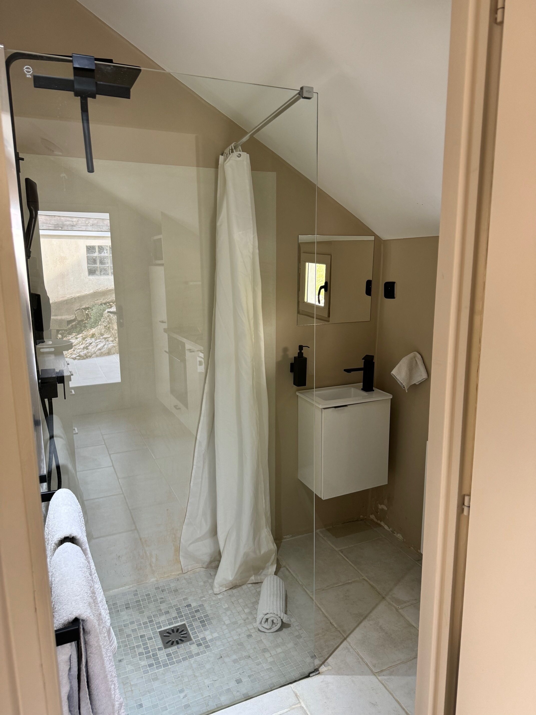 A modern bathroom with a glass shower enclosure, a white sink, and a mirror.
