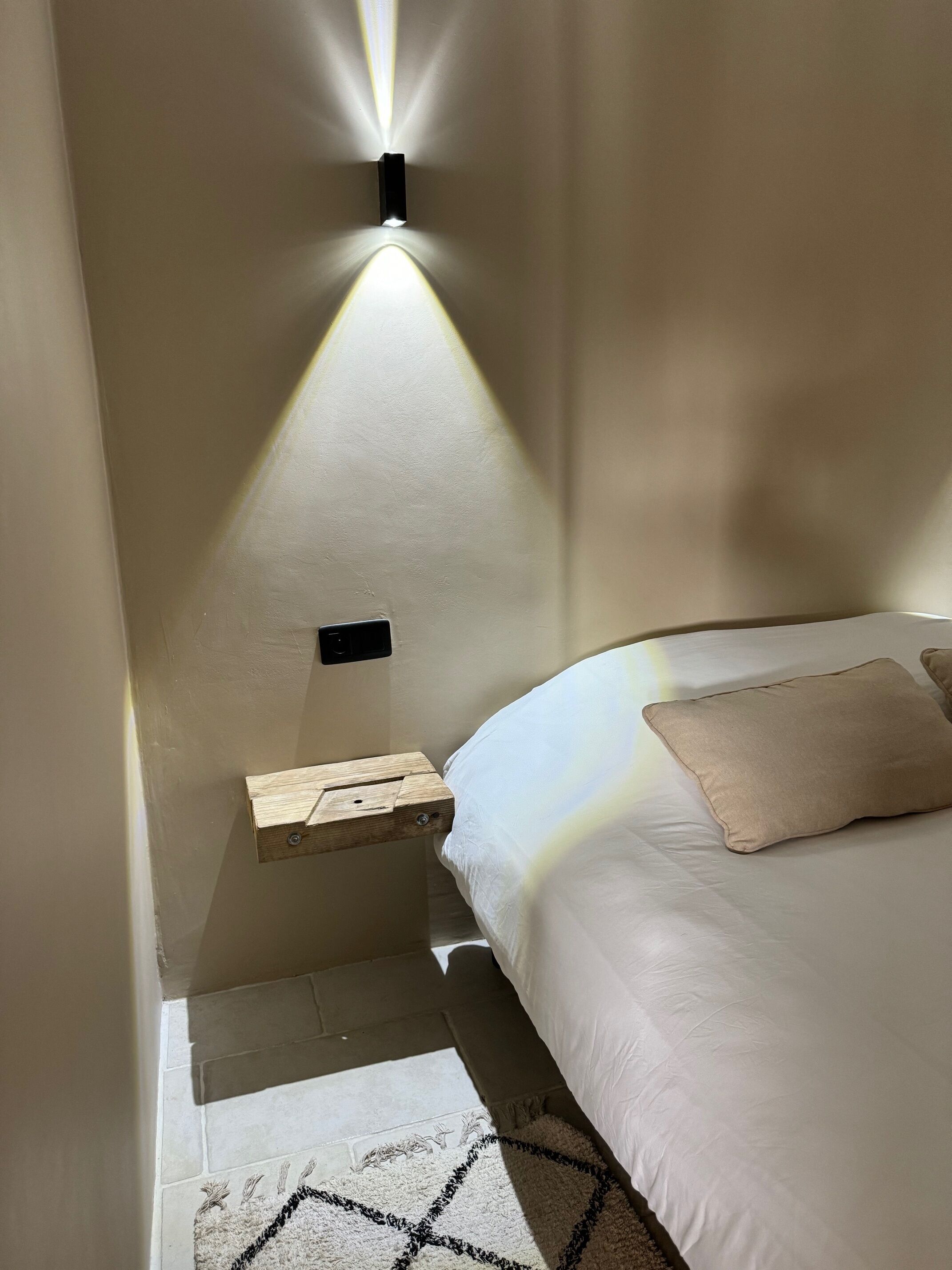 Une chambre à coucher avec un lit, une table de chevet et un luminaire fixé au mur.
