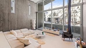 A modern living room with a large window, a sofa, a coffee table, and a fireplace. - Architectural Gem by InvitedHome | Ski-In, Sauna, Patio, Firepit, Unique (Alta)