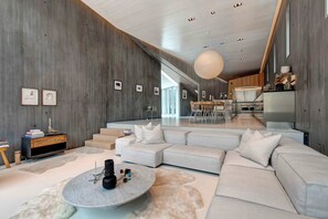Relax in a spacious living area with a large sofa, coffee table, and pendant light, surrounded by artwork and a wooden accent wall.