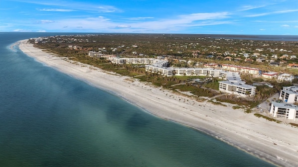 An aerial view of a coastal resort with beachfront properties, a sandy beach, and a clear blue sky.