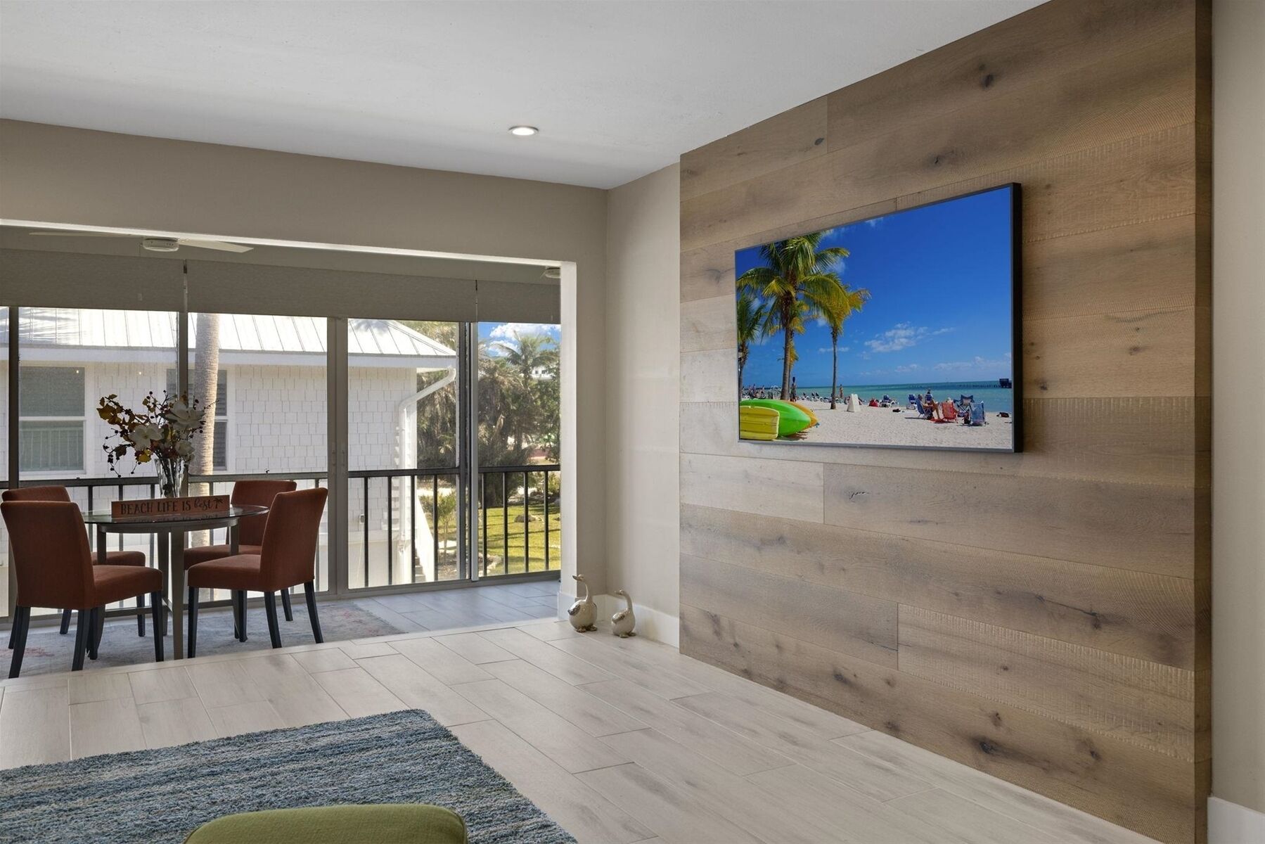 Ein geräumiger Wohnbereich mit Balkon, einem Esstisch mit Stühlen und einem Wandbild im Strandhausstil.