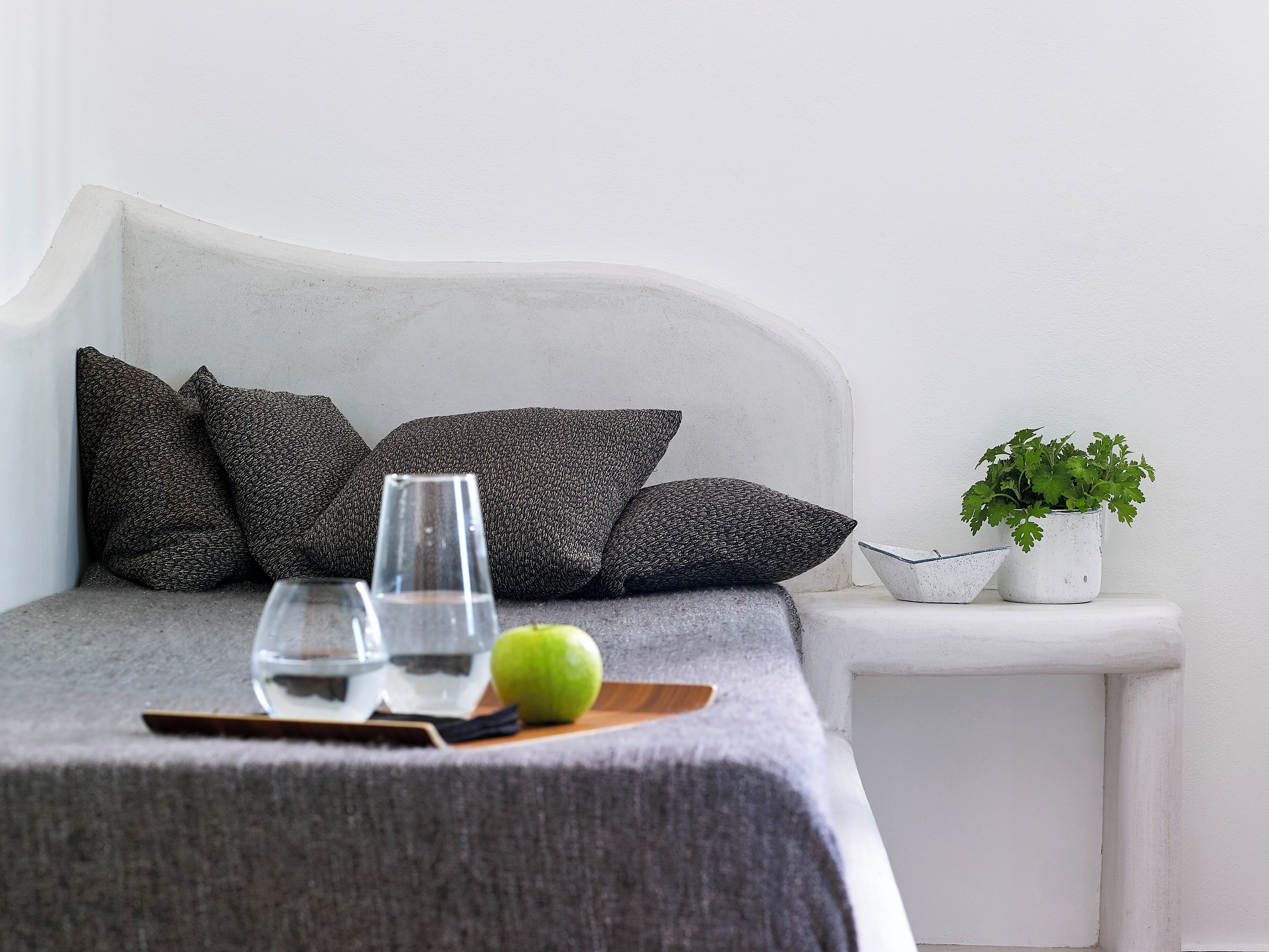Un lit bien fait, avec des oreillers, un verre d’eau, une pomme verte et une petite plante en pot.
