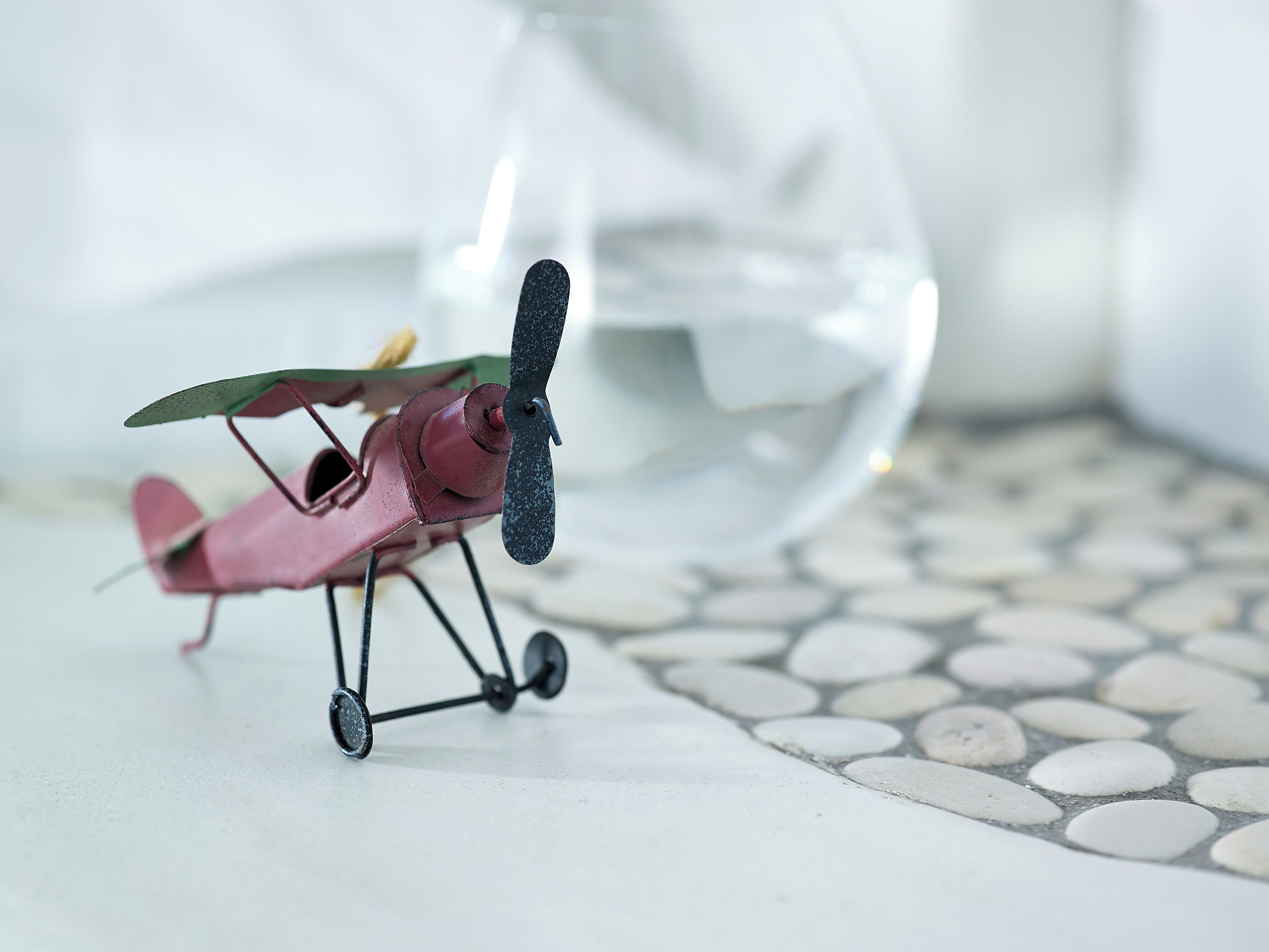A small red biplane model on a tiled floor.