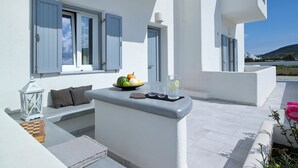 Een moderne buitenzitplek met een tafel gedekt voor twee personen, een schaal fruit en een waterkan.