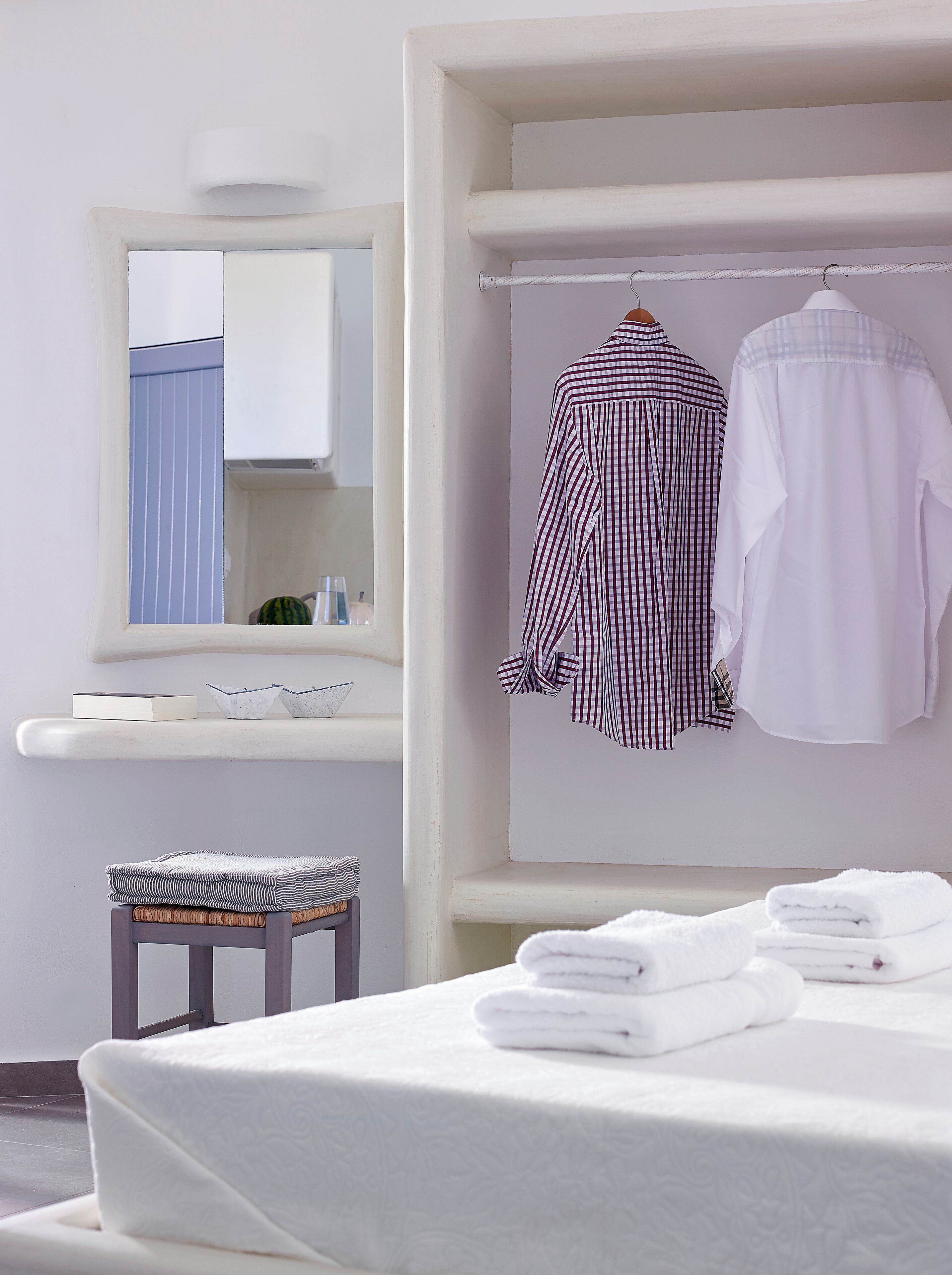 A bathroom with a white sink, a mirror, a towel rack with folded towels, and a small stool with a striped cushion.