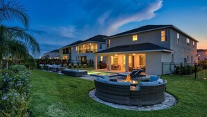 A modern two-story house with a well-maintained lawn, a circular outdoor seating area with a fire pit, and a covered patio. - Luxury Private Pool, Spa, Game Room - 15 min Disney! Free Pool Heat + BBQ (Kissimmee)