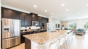 A modern kitchen with dark cabinets, stainless steel appliances, and a granite countertop. - Luxury Private Pool, Spa, Game Room - 15 min Disney! Free Pool Heat + BBQ (Kissimmee)
