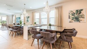 A spacious dining area with a large table and modern chairs, a chandelier, and a large window with curtains. - Luxury Private Pool, Spa, Game Room - 15 min Disney! Free Pool Heat + BBQ (Kissimmee)