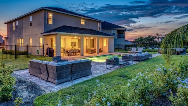 A two-story house with a covered patio, a swimming pool, and outdoor seating. - Luxury Private Pool, Spa, Game Room - 15 min Disney! Free Pool Heat + BBQ (Kissimmee)