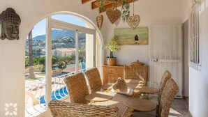 A cozy room with wicker furniture, a view of the mountains, and a painting on the wall. - Villa VENTURA by Abahana Villas (Calpe)