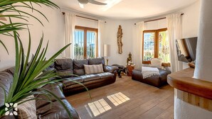 A living room with a ceiling fan, leather sofas, a Buddha statue, and a TV. - Villa VENTURA by Abahana Villas (Calpe)