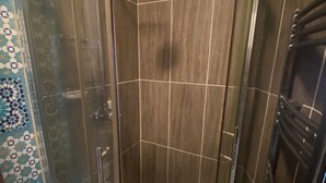 Eine gläserne Duschkabine mit Handbrause, geflieste Wände und einem gemusterten Boden.