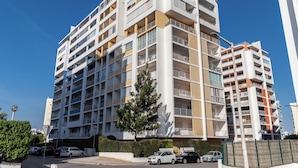 A multi-story residential building with balconies, a parking area, and a clear blue sky. - Rorippa Apartment, Portimao, Algarve (Portimão)