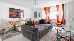 A modern living room with a grey sofa, orange curtains, and a cityscape painting.