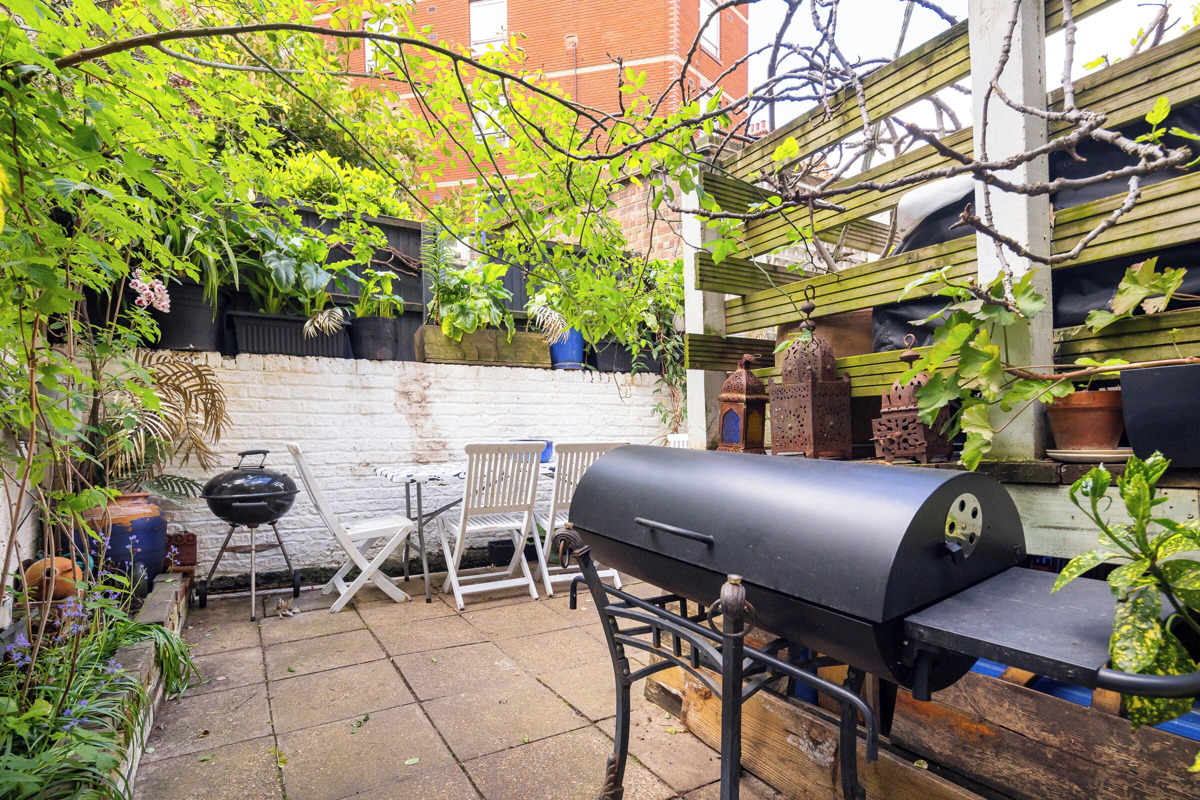 A backyard with a barbecue grill, outdoor furniture, and potted plants.