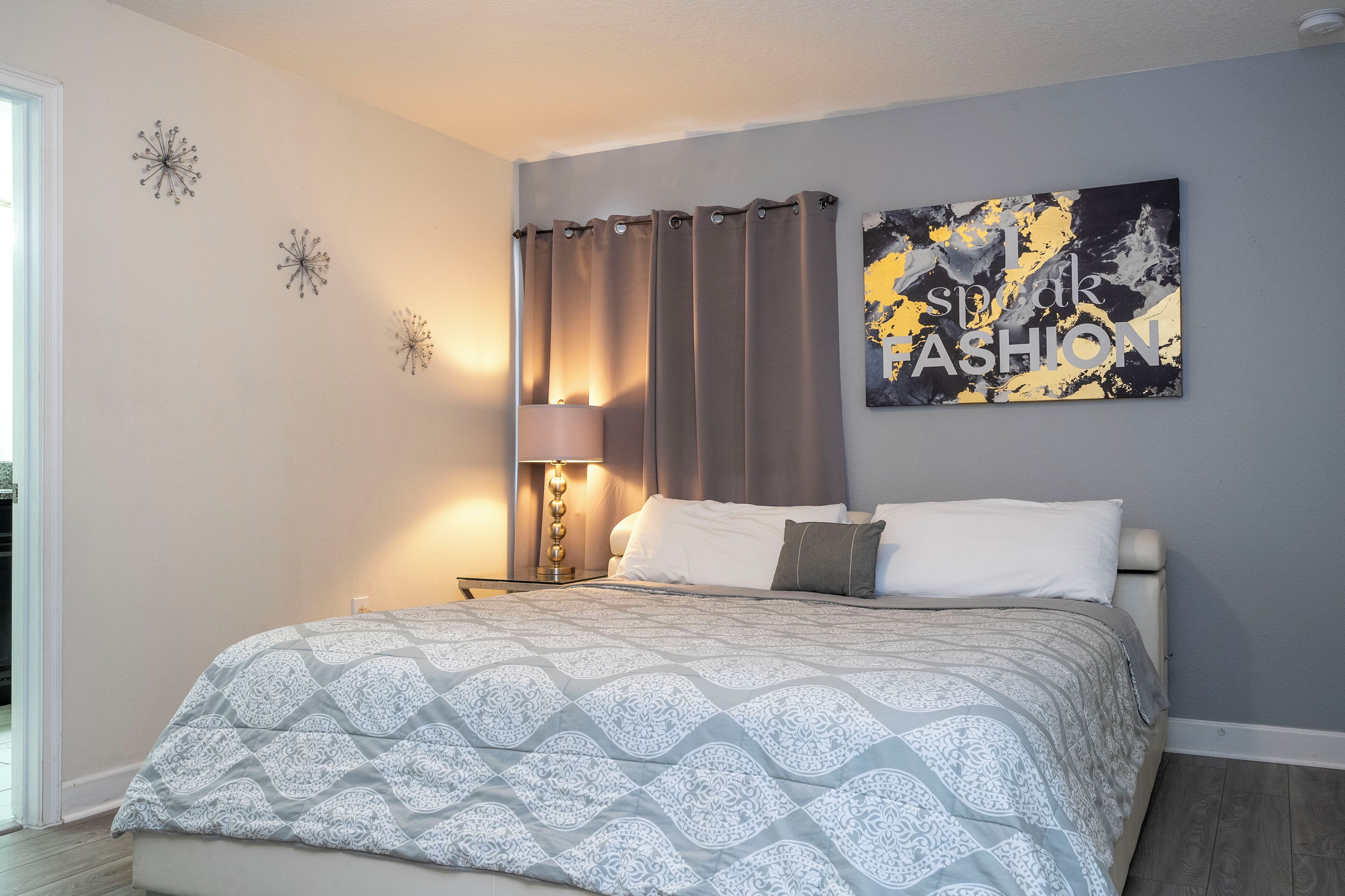 Un dormitorio con cama, mesita de noche, lámpara y un cuadro en la pared.