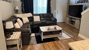 A living room with a leather sofa, a coffee table, a TV, and a bookshelf. - Charming 2-bedroom townhome with WiFi, AC/Heat in delightful Billings (Billings)