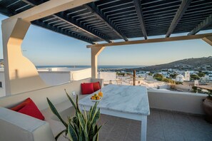 Una terraza con una mesa blanca, cojines rojos y una planta en maceta.