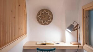 Un espacio de estudio con un escritorio de madera, una silla azul, un libro abierto, una lámpara de escritorio y un adorno en la pared.