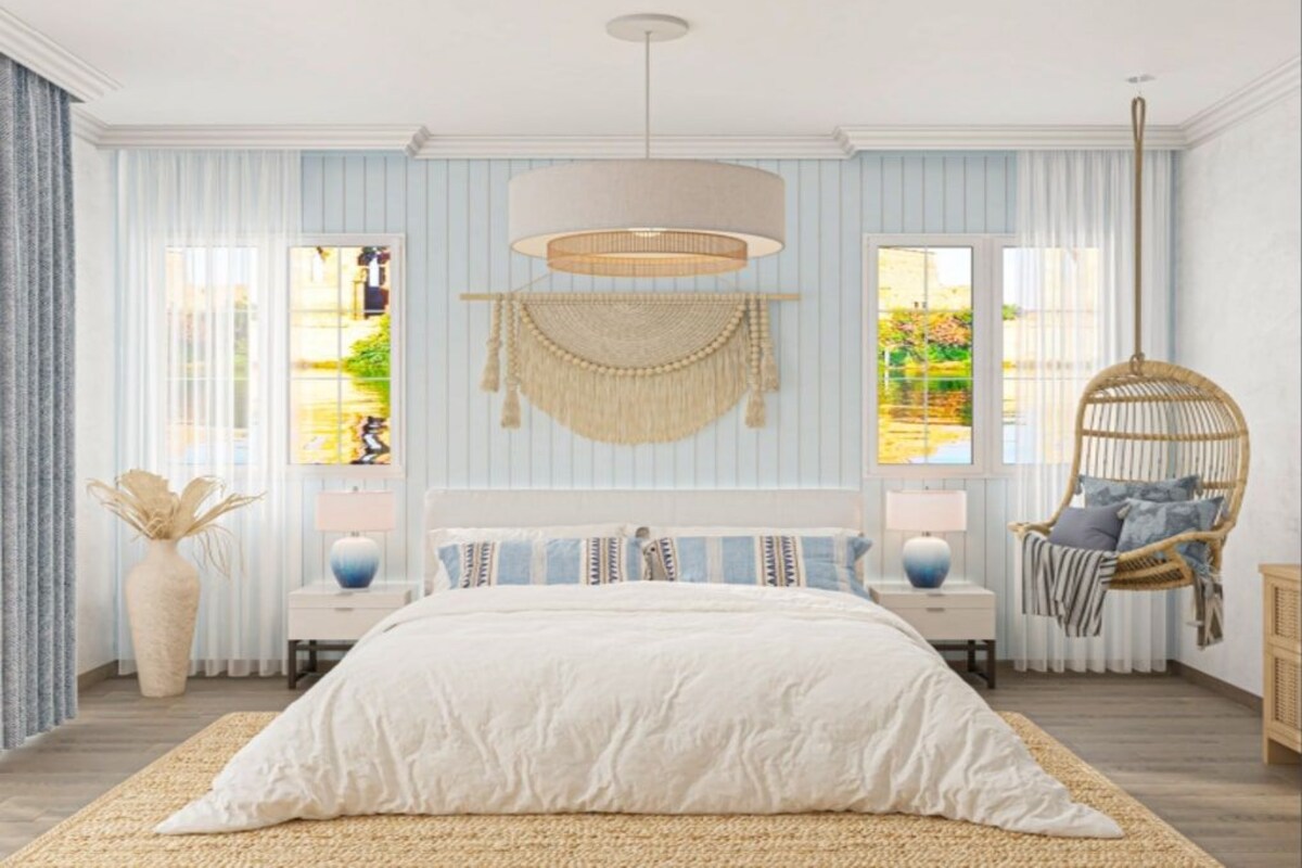 A bedroom with a large bed, two bedside tables, a hanging lamp, a wicker chair, and a view of greenery outside.