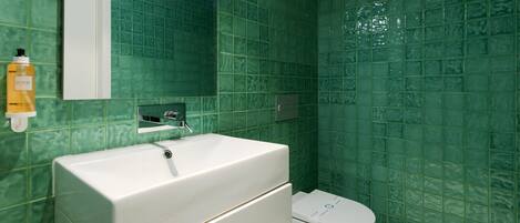 A bathroom with green tiled walls, a white sink, and a toilet.