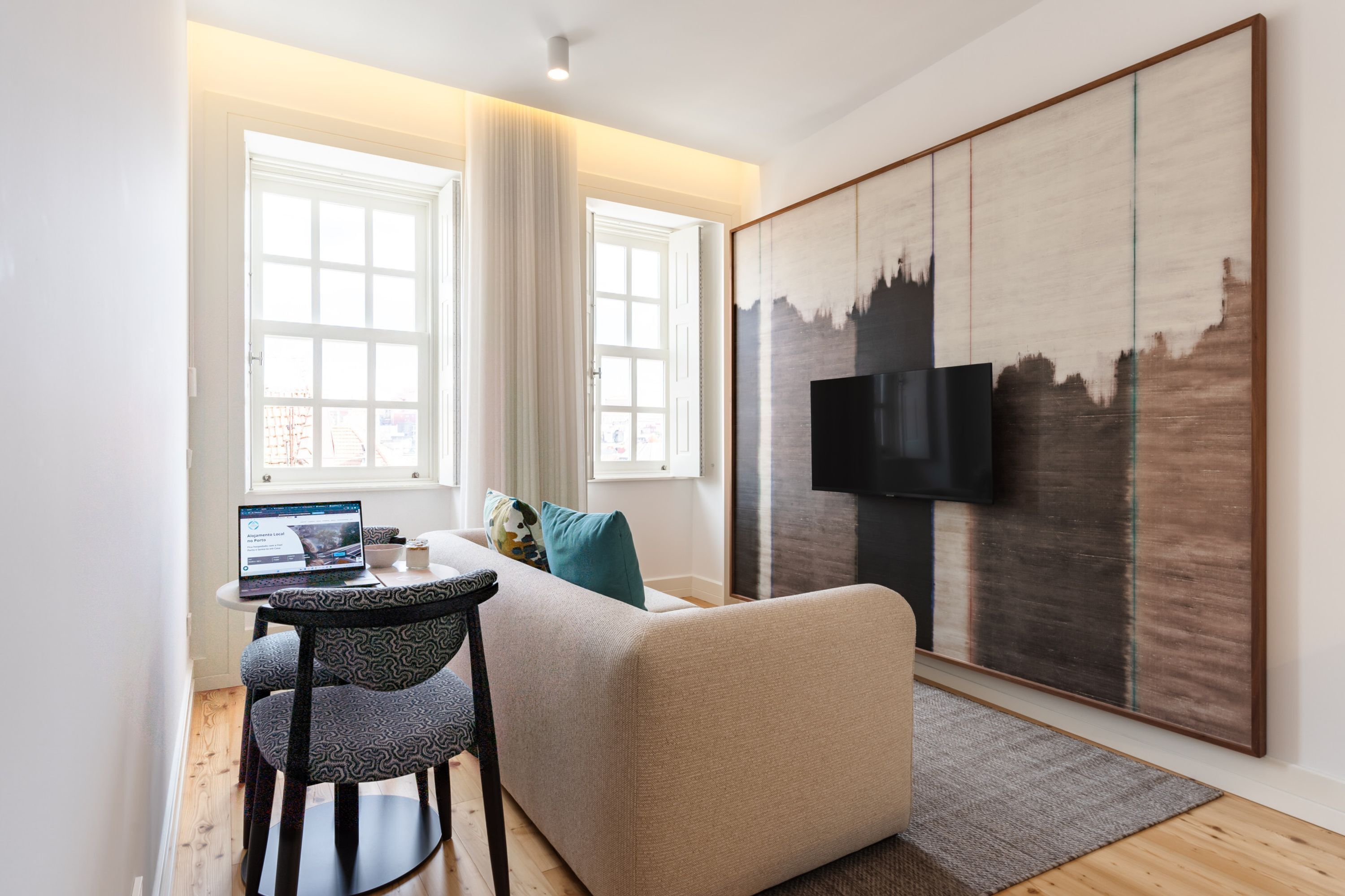 A modern living room with a sofa, a coffee table, a laptop, and a TV mounted on the wall.