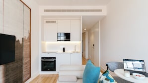 A modern apartment with a kitchenette, a sofa with cushions, a dining table with a laptop, and a TV mounted on the wall. - Feel Porto Cl Rigos Charm Flat 3 3 (Porto)