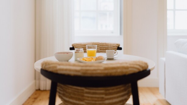 Mesa de café da manhã com uma tigela, um copo de suco de laranja, uma xícara e um prato de comida.