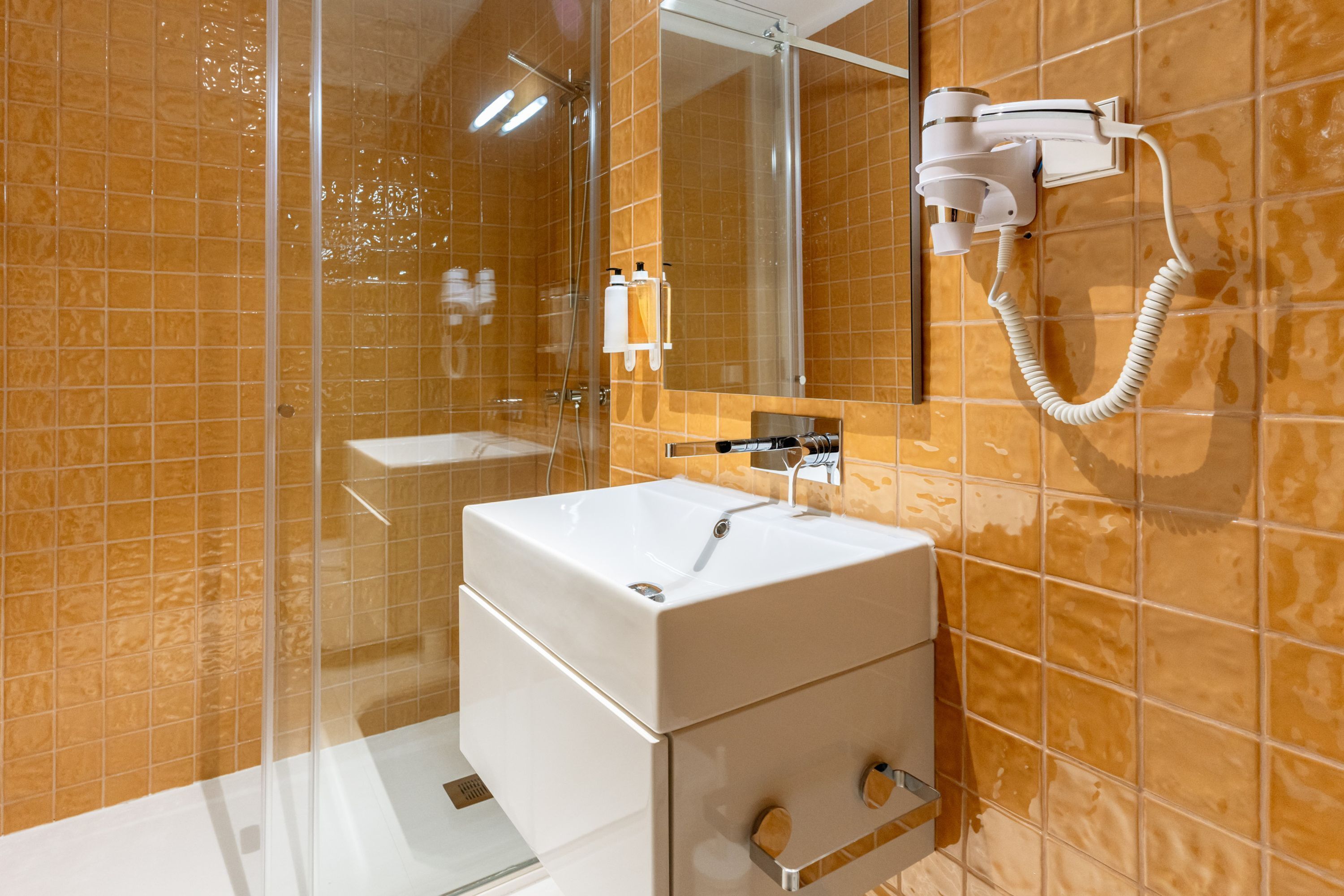 Un bagno con box doccia in vetro, lavandino bianco e asciugacapelli montato a parete.
