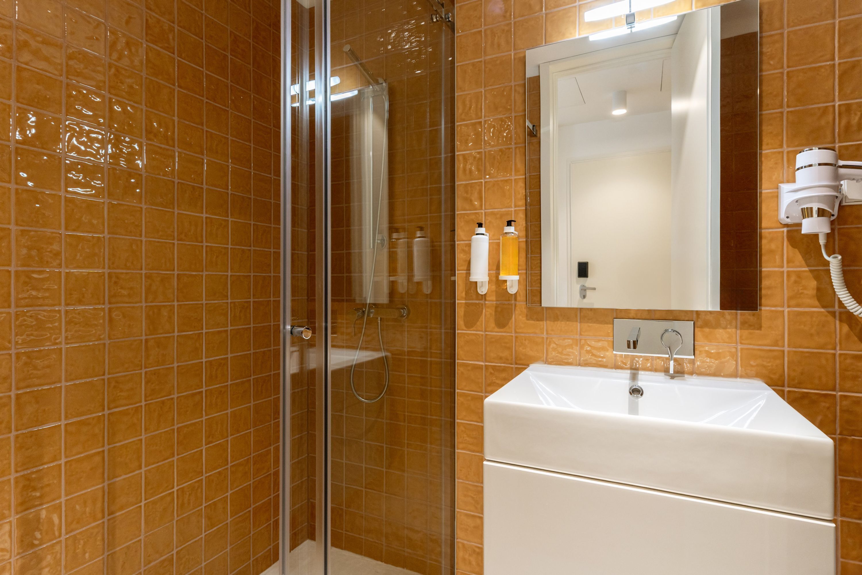Een badkamer met een douchecabine van glas, een wit wastafelmeubel en een aan de muur bevestigde haardroger.