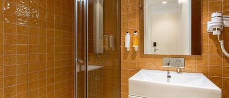 A bathroom with a glass shower enclosure, a white sink, and a hairdryer mounted on the wall.