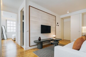 Una sala de estar moderna con un televisor de pantalla plana montado en la pared, un sofá con un cojín naranja y una mesa de centro.