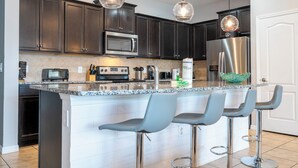 Una cocina moderna con armarios oscuros, electrodomésticos de acero inoxidable, encimera de granito y taburetes de bar.