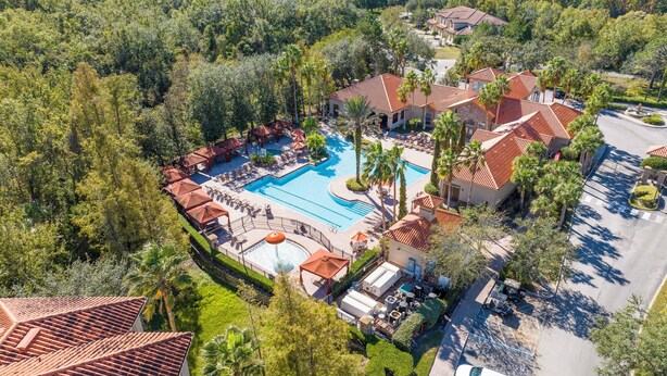 An aerial view of a resort with a central swimming pool, multiple lounge areas, and a parking lot.