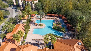 An aerial view of a resort with a central swimming pool, lounge areas, and a parking lot.