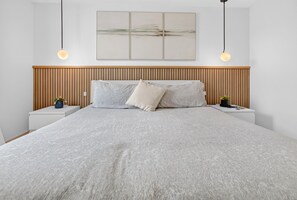 Un dormitorio moderno con una cama grande, cabecero de madera, mesitas de noche con plantas y una obra de arte en la pared.