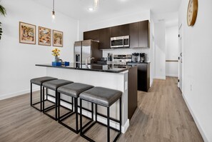 Une cuisine moderne dotée d’un îlot central, de tabourets de bar, d’appareils électroménagers en acier inoxydable et d’un four à micro-ondes placé au-dessus de l’îlot.
