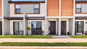 A modern townhouse with a flat roof, large windows, and a small patio area with outdoor seating.