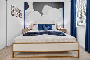 Une chambre à coucher avec un lit, des tables de chevet, un mur décoré de motifs de nuages et des coussins à l’effigie de Mickey Mouse.