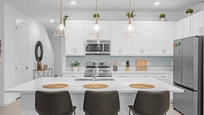 A modern kitchen with white cabinets, a stainless steel refrigerator, and a central island with three chairs.