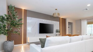 A modern living room with a large TV, a sofa, a potted plant, and a decorative light fixture.
