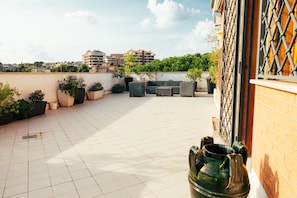 A rooftop terrace with tiled flooring, outdoor furniture, potted plants, and a view of surrounding buildings. - Sunset Apartment in Rome (Rome)