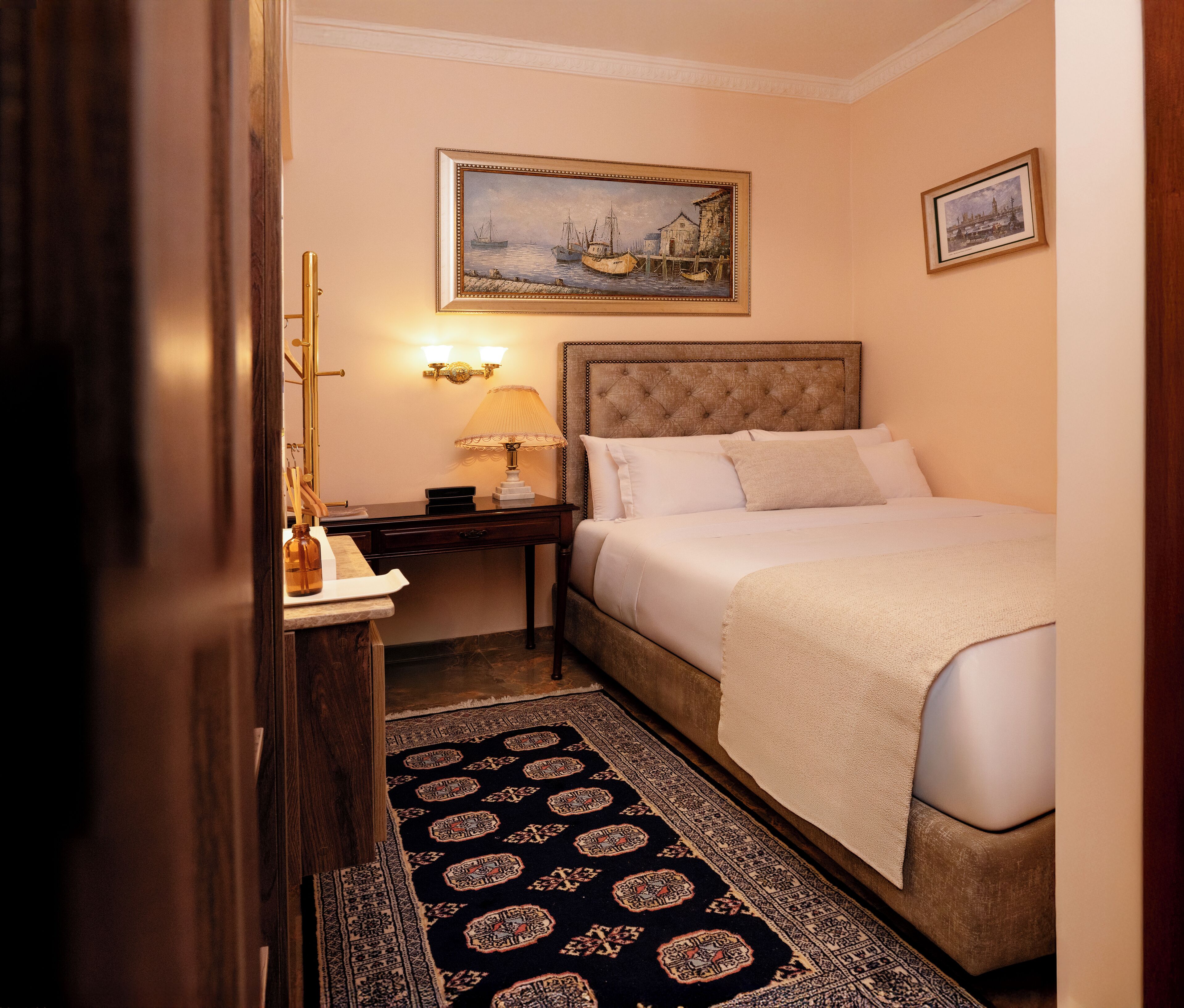 A hotel room with a bed, nightstand, lamp, and a painting on the wall.